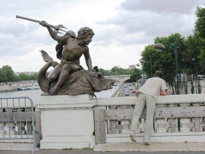 Foto Divertente: Uomo affacciato dal ponte con statua 
