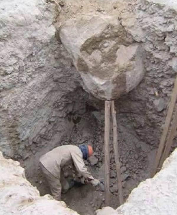 Uomo che lavora in una buca con un legno che regge un masso
