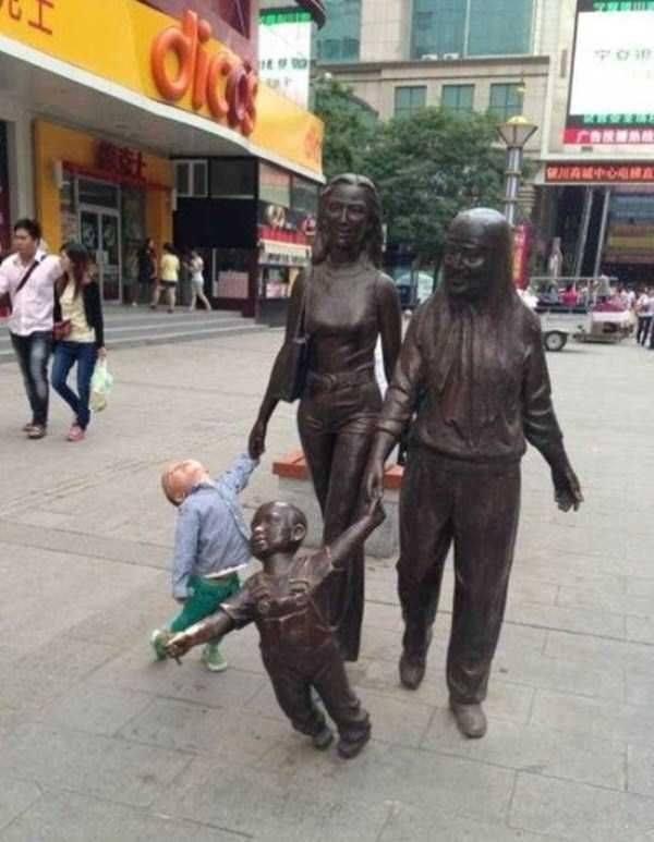 Foto Divertente: Bambino che prende per mano due statue