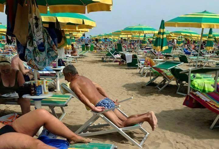 Foto Divertente: Uomo seduto al contrario sulla sdraia al mare 